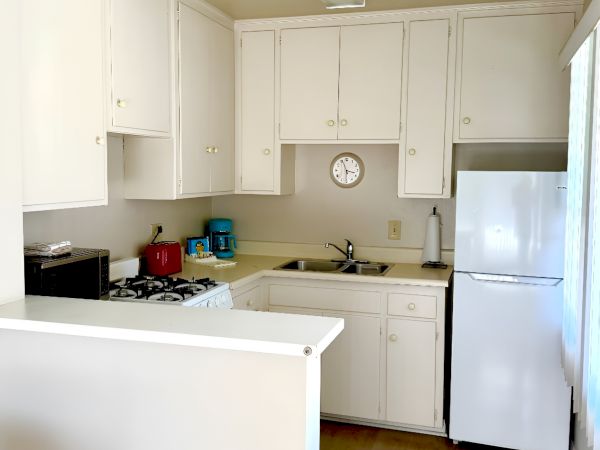 A small white kitchen with cabinets, a stove, sink, toaster, small appliances, and a white fridge, compact and bright.