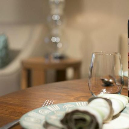 A dining table set with a napkin, plate, and cutlery, a bottle of red wine, a wine glass, and a seashell decor item on the side.